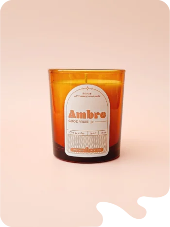 Bougie artisanale parfumée Ambre dans un verre ambré, sur fond rose. Une touche orientale et chaleureuse pour un intérieur cosy.