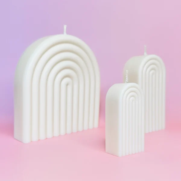 Ensemble de bougies artisanales en forme d’arche, blanches, sur fond rose et violet, créant une ambiance moderne et apaisante.