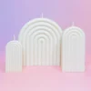 Trio de bougies Happy Arche en cire naturelle, design moderne en forme d’arche, sur fond rose et violet pour une décoration élégante et minimaliste.
