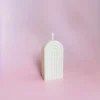 Bougie sculptée Happy Arche taille S en cire naturelle, au design minimaliste, posée sur un fond rose pour une ambiance douce et cosy.
