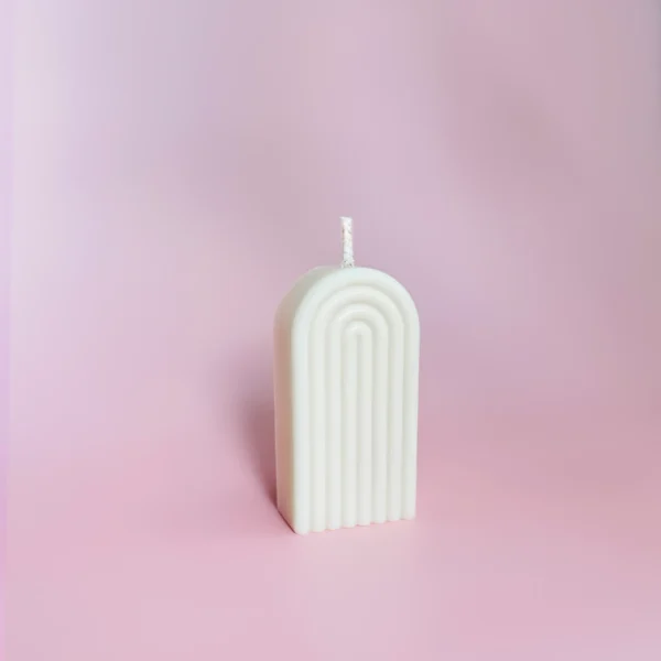 Bougie sculptée Happy Arche taille S en cire naturelle, au design minimaliste, posée sur un fond rose pour une ambiance douce et cosy.