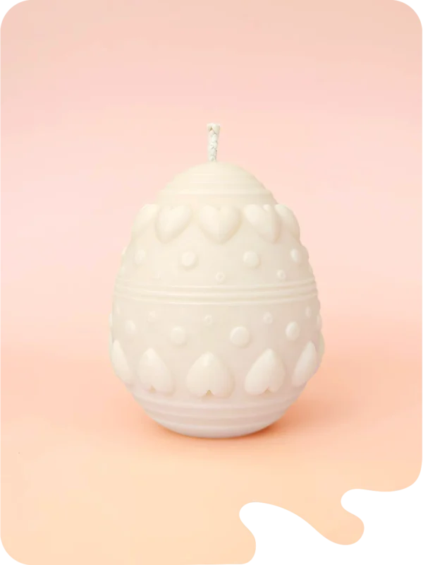 Bougie décorative en forme d’œuf avec motifs cœurs et reliefs, en cire naturelle, présentée sur fond pastel.