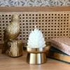 Bougie décorative Pompom Pinewood en forme de pomme de pin, création artisanale Crème Brûlée, présentée dans une déco dorée de Noël.