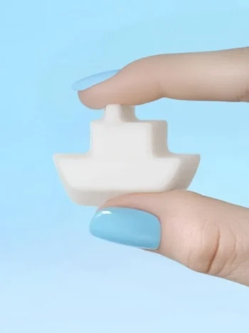 Fondant parfumé en forme de bateau tenu entre deux doigts vernis bleu, sur fond bleu pastel.