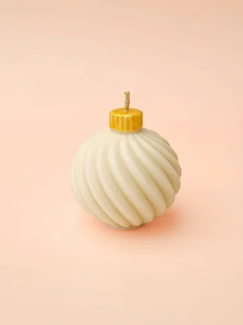 Bougie Bubble Glow | Crème Brûlée Bougie décorative Bubble Glow en cire naturelle, forme boule torsadée avec capuchon doré, présentée sur fond rose pastel.