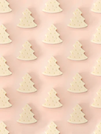 Fondants parfumés Forest en forme de sapin, parfum bois de santal, présentés en motif répétitif sur un fond rose pastel.