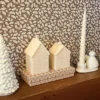 Bougies décoratives en forme de maison, présentées sur une étagère dans une ambiance de Noël naturelle et chaleureuse.