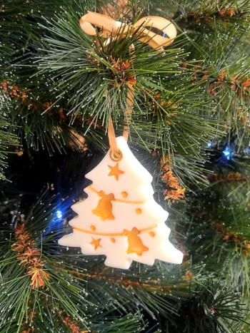 Suspension en cire parfumée en forme de sapin avec détails dorés, accrochée dans un arbre de Noël.
